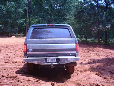 1996 Ford Bronco - A gray Ford Bronco is seen from the rear, stuck in mud with trees in the background.