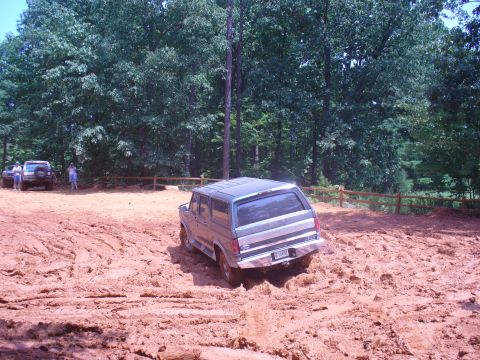 1996 Ford Bronco - A Ford Bronco tackles a challenging muddy terrain, with other vehicles and spectators in the background.