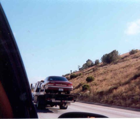 1992 Ford Crown Victoria - Snapshot taken through a car window on a freeway, showing a dark red Ford Crown Victoria sedan strapped to a flatbed tow truck ahead. Dry g…