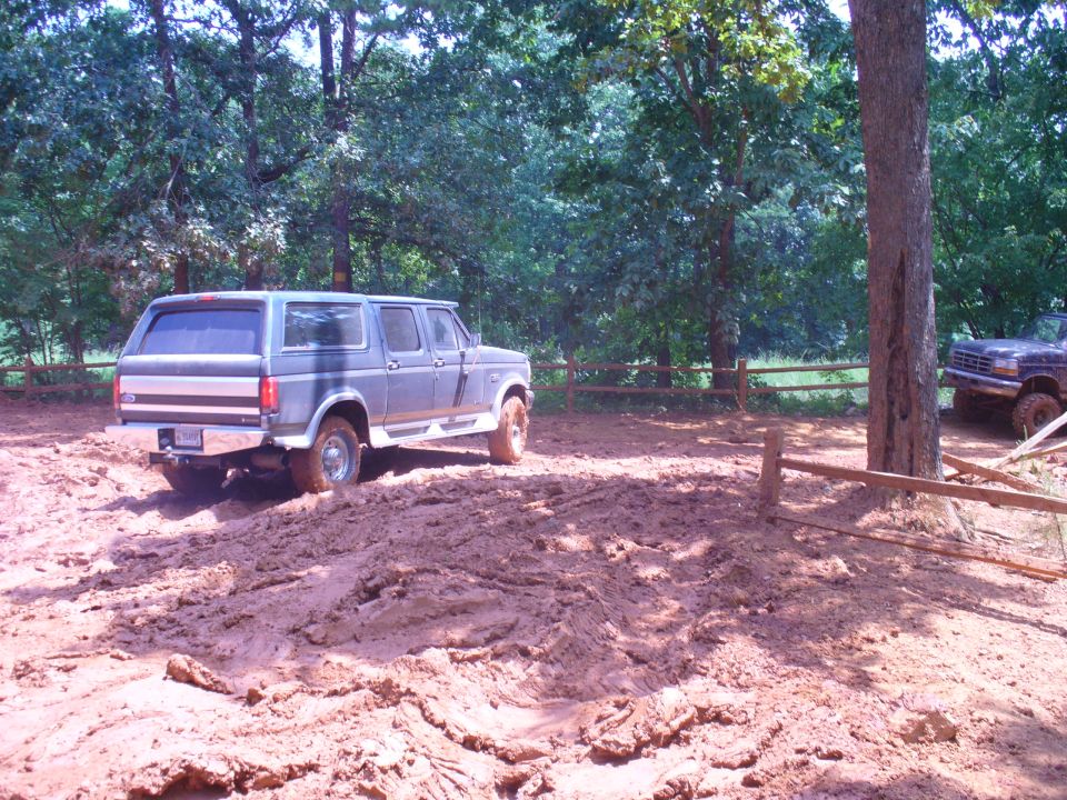 1996 Ford Bronco driving through mud with another vehicle visible in the background