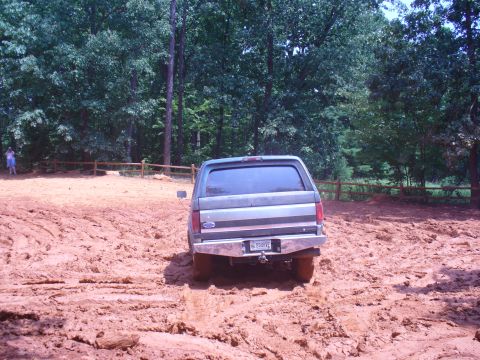 1996 Ford Bronco - A gray Ford Bronco navigates a muddy terrain with trees in the background.