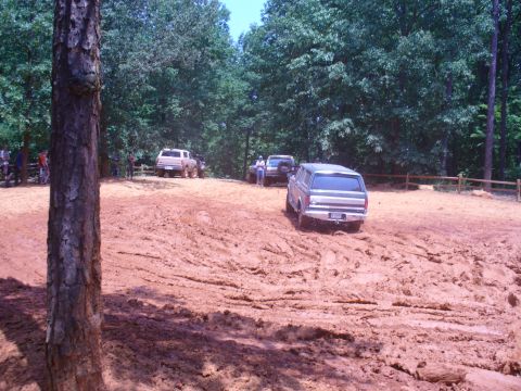 1996 Ford Bronco - Several SUVs navigate a muddy off-road course surrounded by trees.