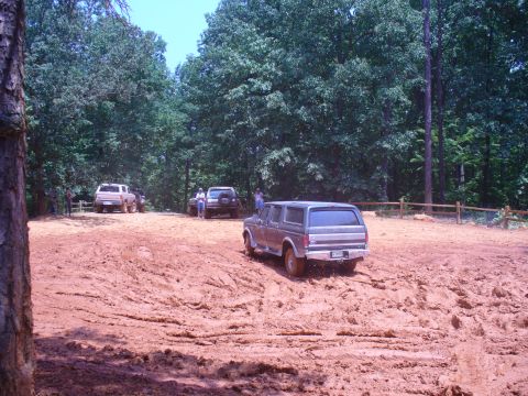 1996 Ford Bronco - Several off-road vehicles navigate a muddy track in a wooded area.