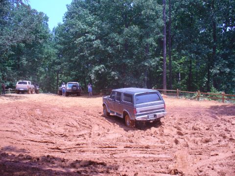 1996 Ford Bronco - Several vehicles navigate a muddy off-road course surrounded by trees.