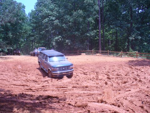1996 Ford Bronco - A dark blue SUV tackles a challenging muddy course, with other vehicles visible in the background.