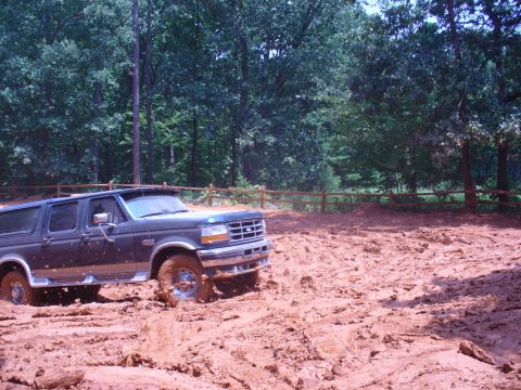 1996 Ford Bronco - Ford Bronco navigating a muddy off-road trail surrounded by trees.