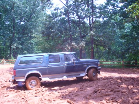1996 Ford Bronco - A blue Ford Bronco is stuck in thick mud on a wooded trail.