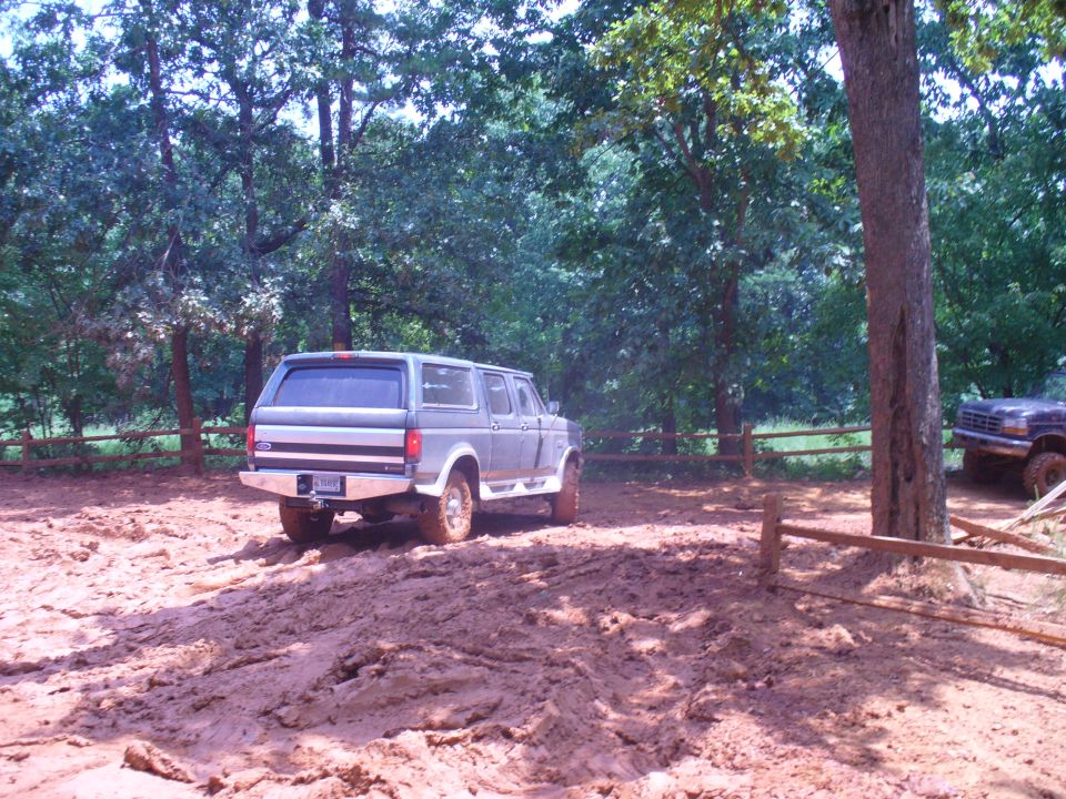 Gray Ford Bronco with a camper shell driving on a muddy track, rear view