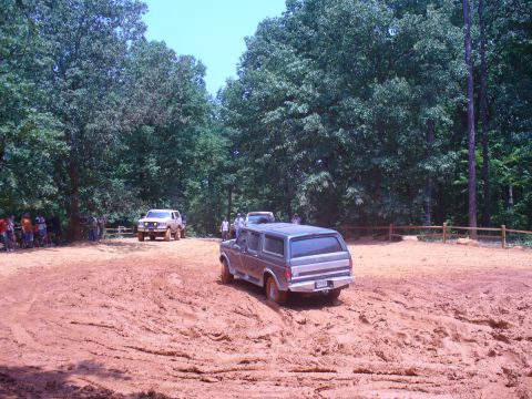 1996 Ford Bronco - A gray Ford Bronco navigates a muddy off-road course with other vehicles and spectators in the background.