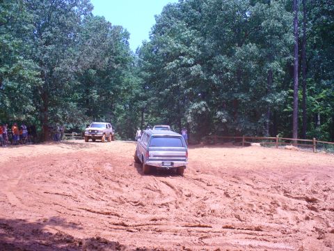 1996 Ford Bronco - A dark SUV navigates a muddy track with another vehicle in the distance, suggesting an off-road event.