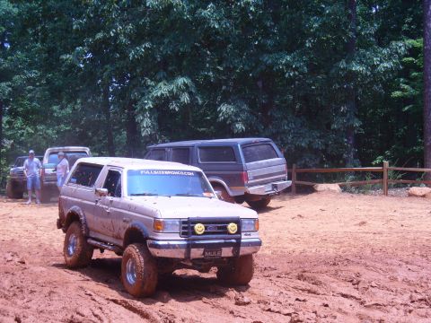 1996 Ford Bronco - Muddy 1996 Ford Bronco navigates off-road terrain with other vehicles present.