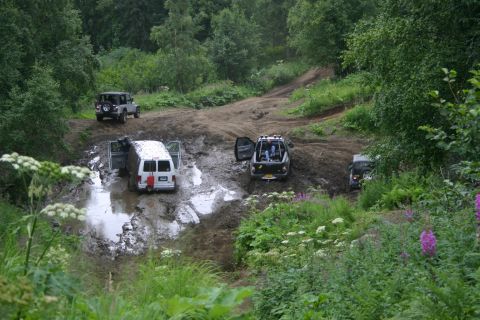 2003 Jeep TJ - Multiple vehicles are stuck in a muddy off-road course, surrounded by lush green vegetation.