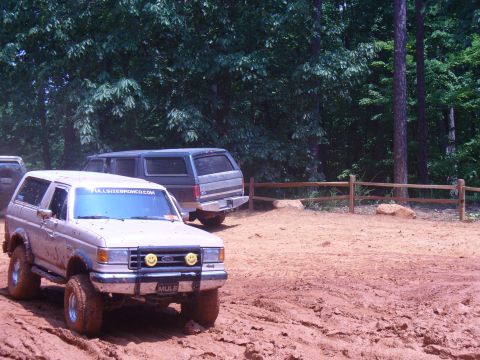 1996 Ford Bronco - This Ford Bronco, likely from the late 1980s, navigates a muddy off-road course with another SUV in the background.