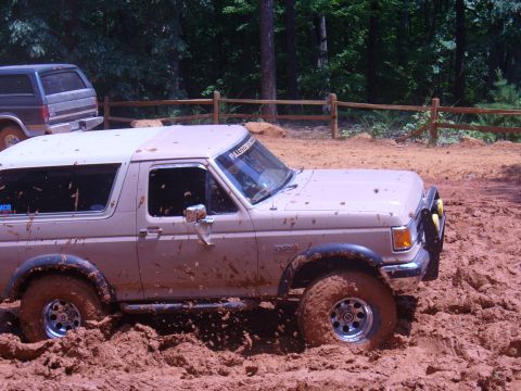 1996 Ford Bronco - Two Ford Broncos navigate a muddy off-road trail during an event.