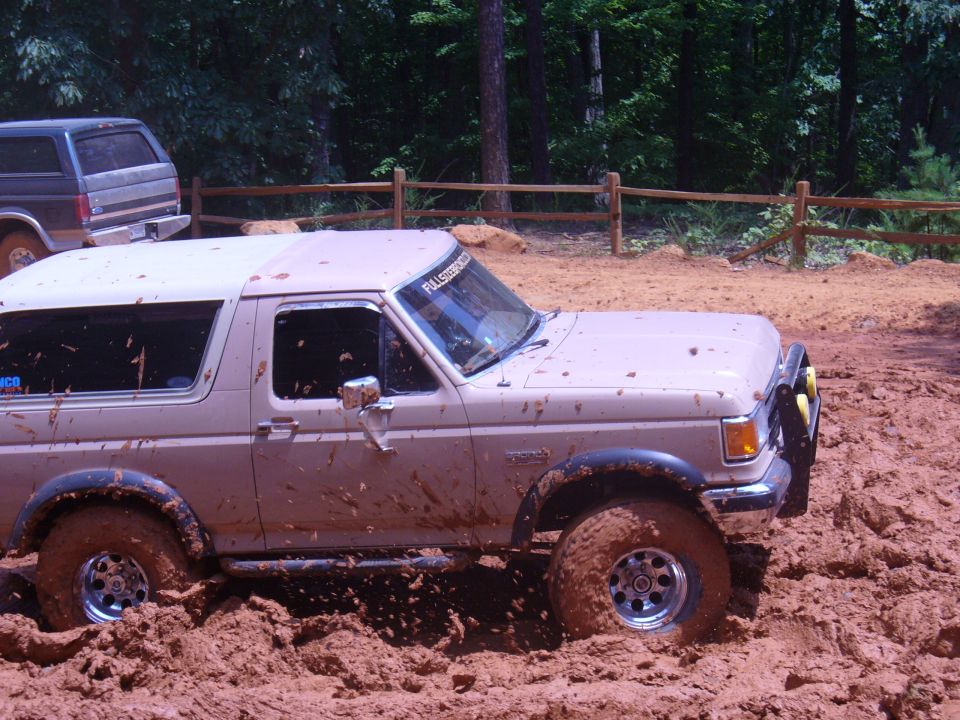 Tan Ford Bronco stuck in thick mud, another Bronco visible behind it