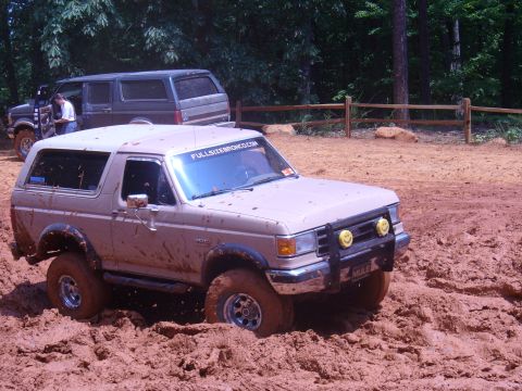 1996 Ford Bronco - A tan Ford Bronco navigates a muddy off-road course with another SUV in the background.