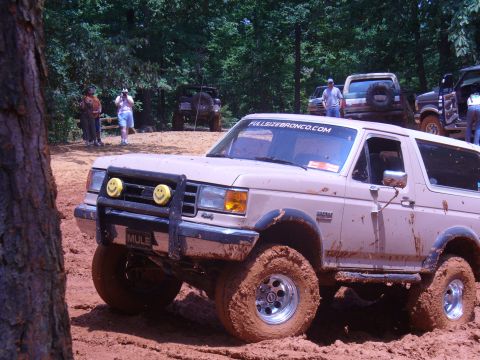 1996 Ford Bronco - A tan Ford Bronco navigates a muddy off-road course, with other vehicles and spectators present.
