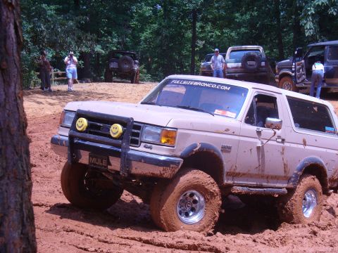 1996 Ford Bronco - Off-roading event shows a 1996 Ford Bronco navigating a muddy trail with other vehicles present.