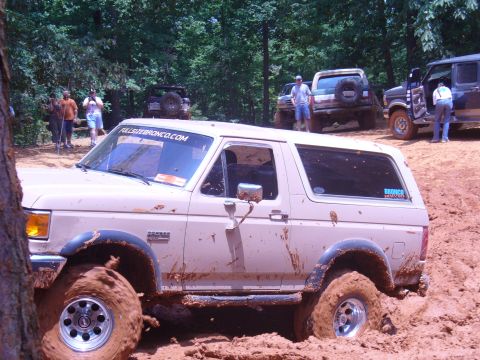 1996 Ford Bronco - Several off-road vehicles navigate a muddy trail during an event.