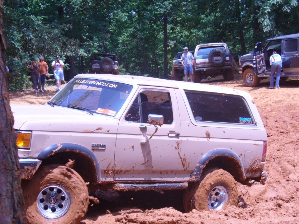 Tan Ford Bronco stuck in mud, side view. Mud splatters cover the vehicle