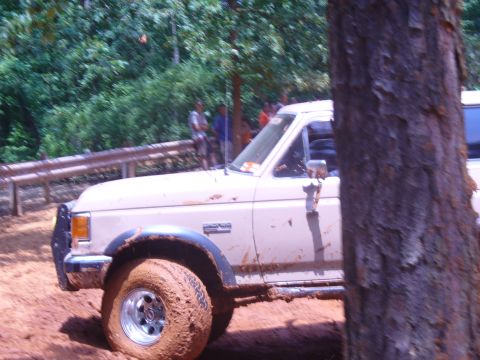 1996 Ford Bronco - Ford Bronco navigates a muddy off-road course with trees and spectators in the background.