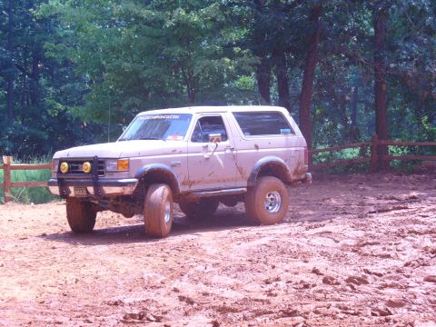1996 Ford Bronco - A mud-covered Ford Bronco navigates a dirt track in a wooded area.
