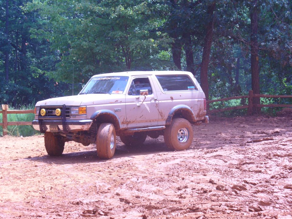 Tan Ford Bronco covered in mud, with off-road tires and yellow fog lights