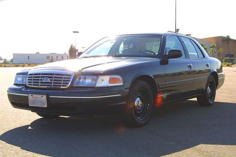 1998 Ford Crown Victoria - A black sedan is viewed from a three-quarter front angle under a bright sky.