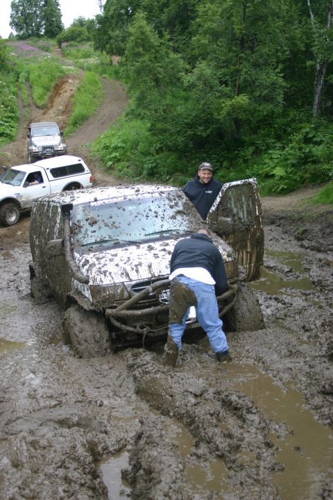 2003 Jeep TJ - Multiple off-road vehicles are mired in deep mud on a trail, with individuals attempting to navigate the difficult terrain.