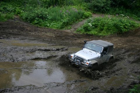 2003 Jeep TJ - A silver 2003 Jeep TJ Wrangler navigates a challenging muddy off-road course, with its tires deep in the mire.