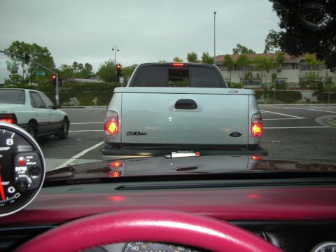 1998 Ford Crown Victoria - Driver's-eye view through a windshield of a silver Ford pickup truck stopped ahead at a traffic light on a wet road.