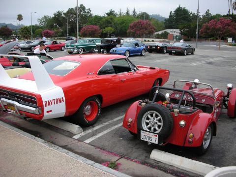 1998 Ford Crown Victoria - red Dodge Charger Daytona with its tall rear wing parked next to a red Lotus-style roadster in a car show lot.