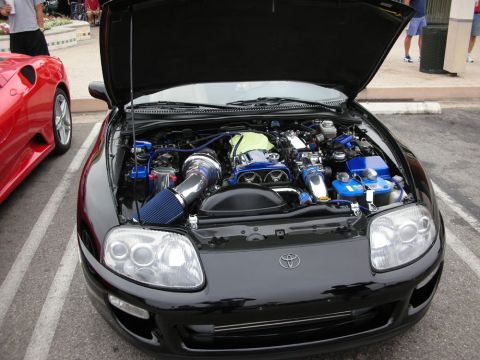 1998 Ford Crown Victoria - Open engine bay of a black Toyota Supra showing a blue twin-turbo inline-six with blue cam covers and an intake.