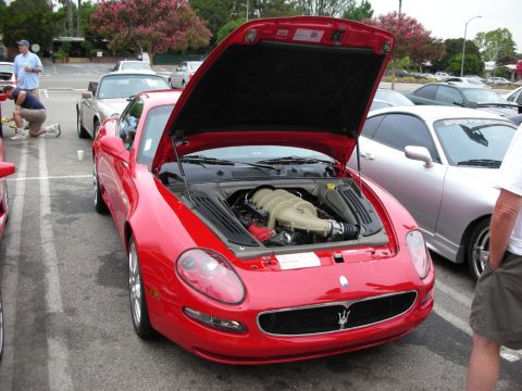 1998 Ford Crown Victoria - red Maserati coupe with its hood raised, exposing the V8 engine, parked among cars at a show.