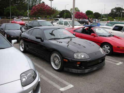 1998 Ford Crown Victoria - black Toyota Supra with a rear wing and chrome multi-spoke wheels parked among sports cars at a show.