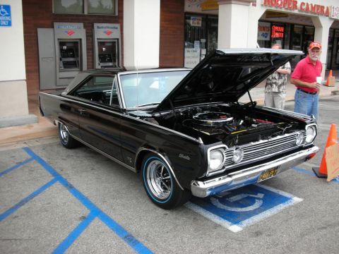 1998 Ford Crown Victoria - black mid-60s Plymouth Satellite hardtop with open hood and chrome wheels parked outside storefronts.