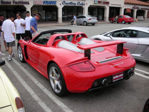 1998 Ford Crown Victoria - red Porsche Carrera GT with rear spoiler and silver wheels parked outside storefronts at a car meet.