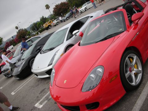 1998 Ford Crown Victoria - lineup of supercars at a meet led by a red Porsche Carrera GT with a white Lamborghini Gallardo behind.