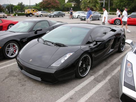 1998 Ford Crown Victoria - black Lamborghini Gallardo with dark wheels parked among other cars at an outdoor car show.