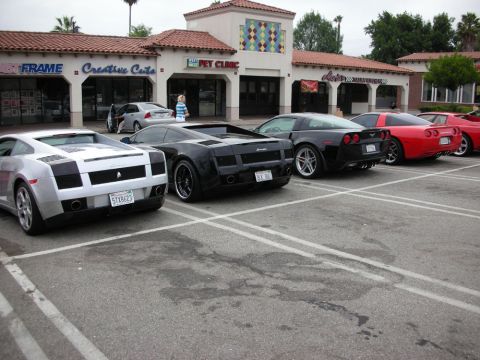 1998 Ford Crown Victoria - Two Lamborghini Gallardos, one silver and one black, parked rear-in next to a red Corvette outside a strip mall with a pet clinic.