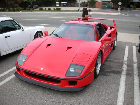 1998 Ford Crown Victoria - red Ferrari F40 with its large rear wing, parked beside a white Porsche while a bystander stands nearby.
