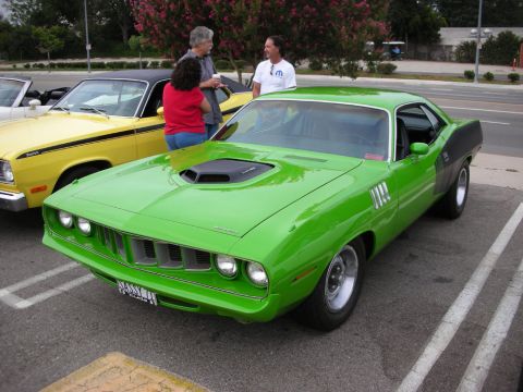 1998 Ford Crown Victoria - bright green vintage muscle-car coupe with a black hood scoop and shaker, parked beside a yellow car as people talk nearby.