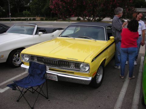 1998 Ford Crown Victoria - yellow vintage muscle coupe with a black side stripe parked in a lot, a blue folding chair set in front and people standing beside it.