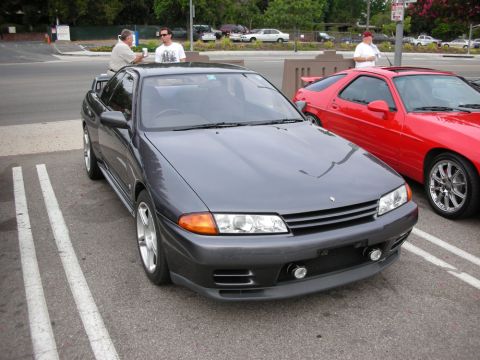 1998 Ford Crown Victoria - gray Nissan Skyline GT-R shown front three-quarter, with a red sports car alongside and spectators in the background.
