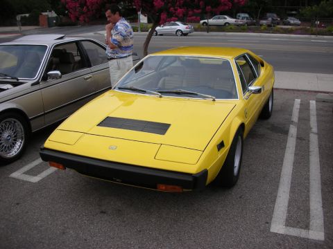 1998 Ford Crown Victoria - yellow 1970s wedge-shaped Ferrari coupe parked at a curb next to a gold BMW sedan, with a man standing beside it.