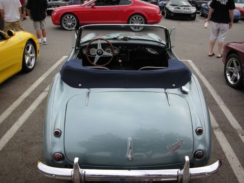 1998 Ford Crown Victoria - rear of a light-blue British roadster with a folded navy top and wood steering wheel, parked among sports cars at a show.