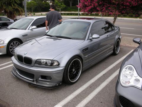 1998 Ford Crown Victoria - gray BMW E46 M3 coupe, lowered on staggered black wheels with a front splitter, parked in a lot beside another silver BMW.