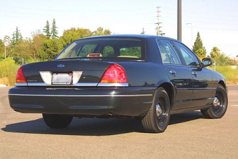 1998 Ford Crown Victoria - dark Ford Crown Victoria sedan with steel wheels viewed from the rear right three-quarter on open pavement with trees behind.