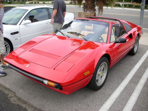 1998 Ford Crown Victoria - red Ferrari 308/328-style targa with tan interior and removable roof panel, parked at a curb beside a white car.