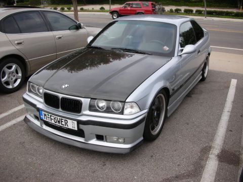 1998 Ford Crown Victoria - silver BMW E36 coupe with a carbon-fiber hood, lowered on black wheels, wearing an 'M POWER' front plate.